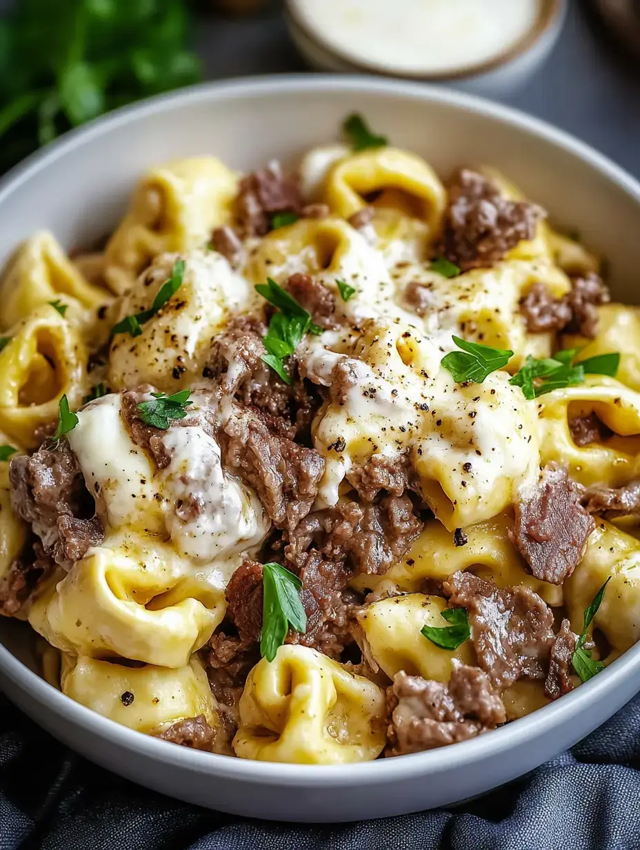 A bowl of creamy tortellini pasta topped with seasoned beef and fresh parsley.