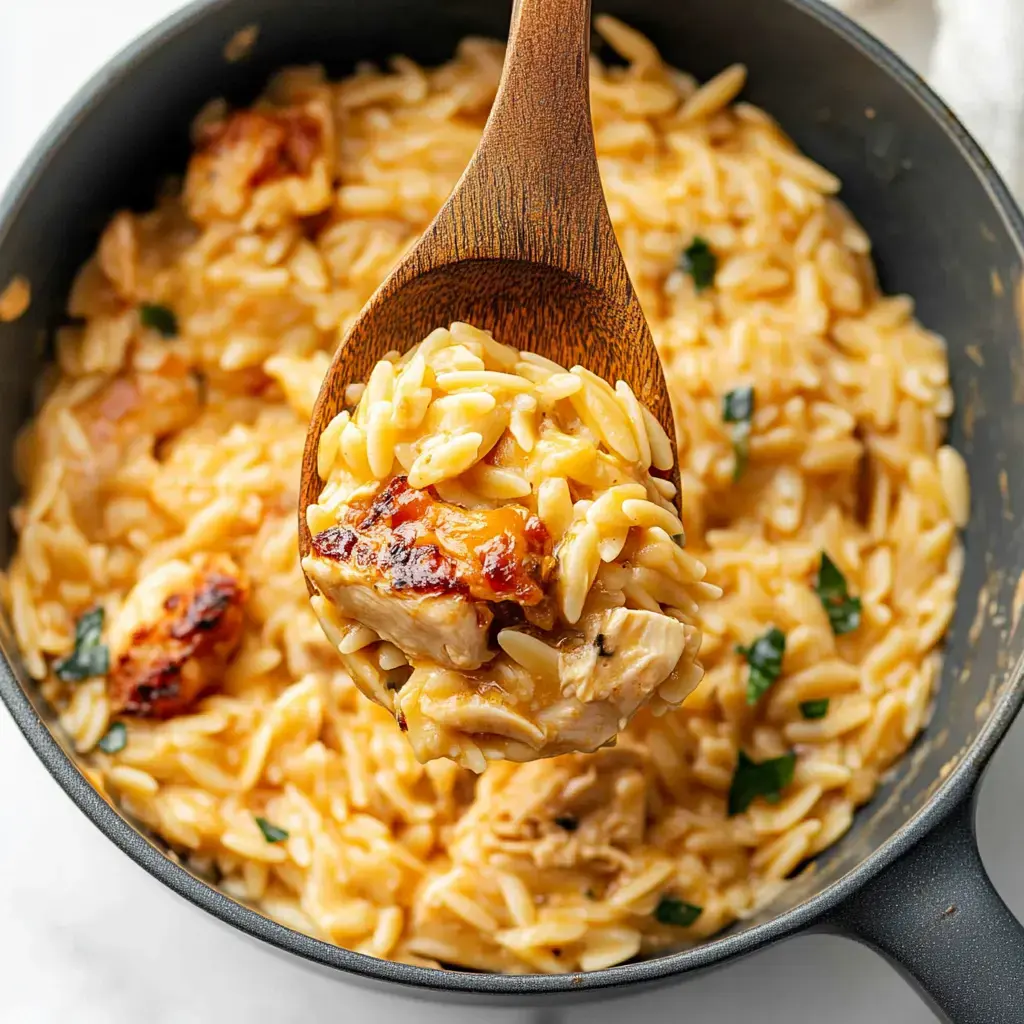 A wooden spoon is lifting a serving of creamy orzo pasta with pieces of chicken from a black pot.