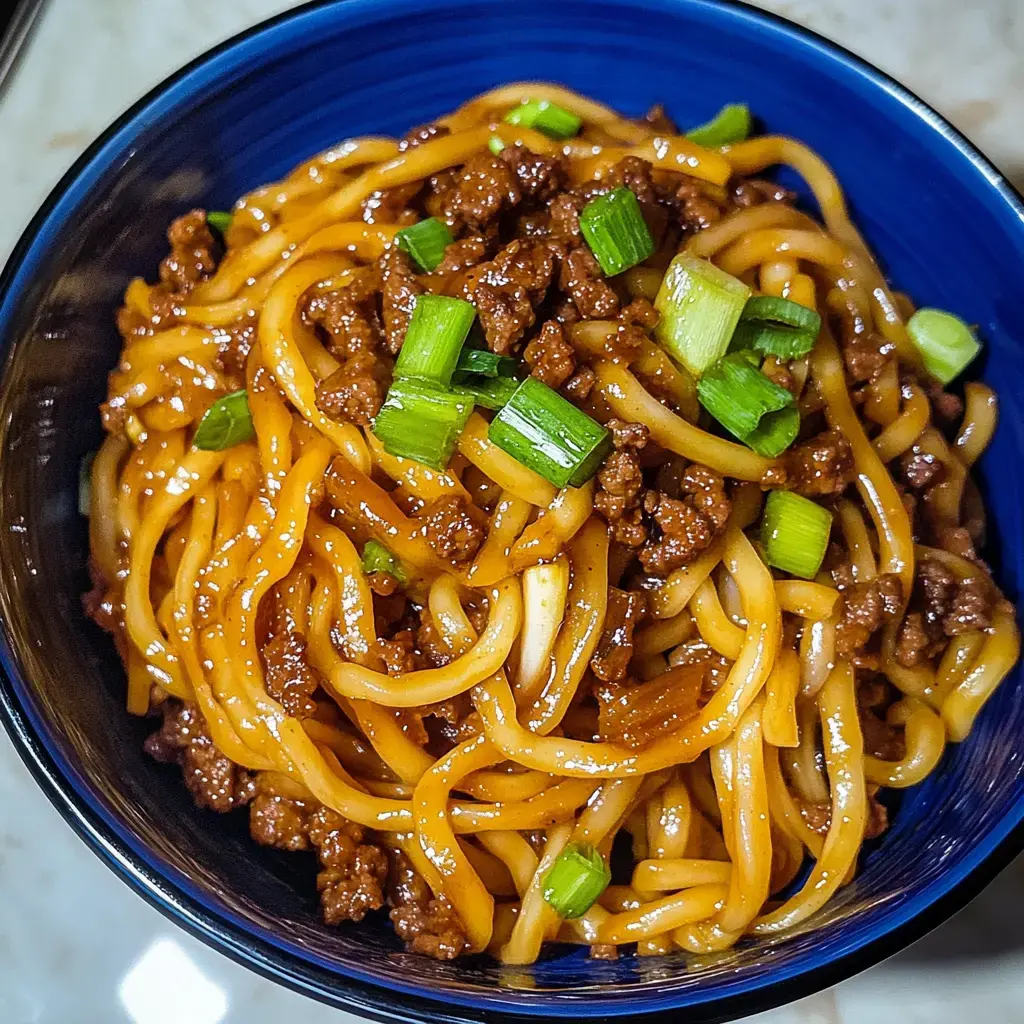 A close-up view of a bowl of noodles topped with ground meat and garnished with chopped green onions.