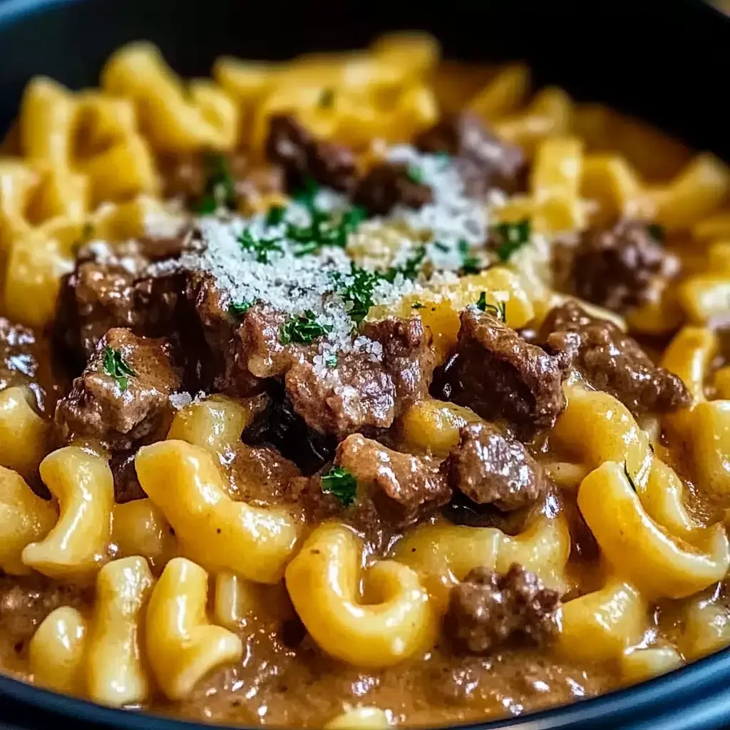 A close-up view of a creamy pasta dish with curvy noodles, tender beef chunks, and a sprinkle of grated cheese and parsley on top.