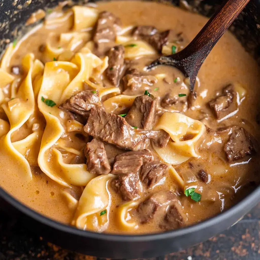 A close-up of beef stroganoff featuring tender beef strips and wide noodles in a creamy brown sauce, garnished with parsley.