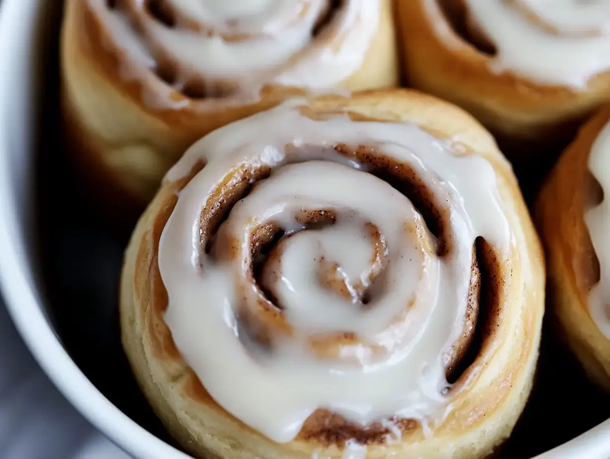 A close-up of freshly baked cinnamon rolls topped with creamy icing.