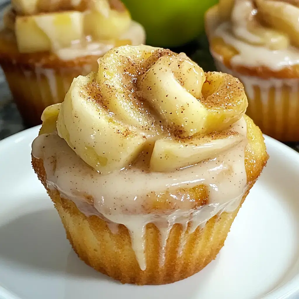 A moist cupcake topped with a swirl of frosting and slices of apple, dusted with cinnamon.