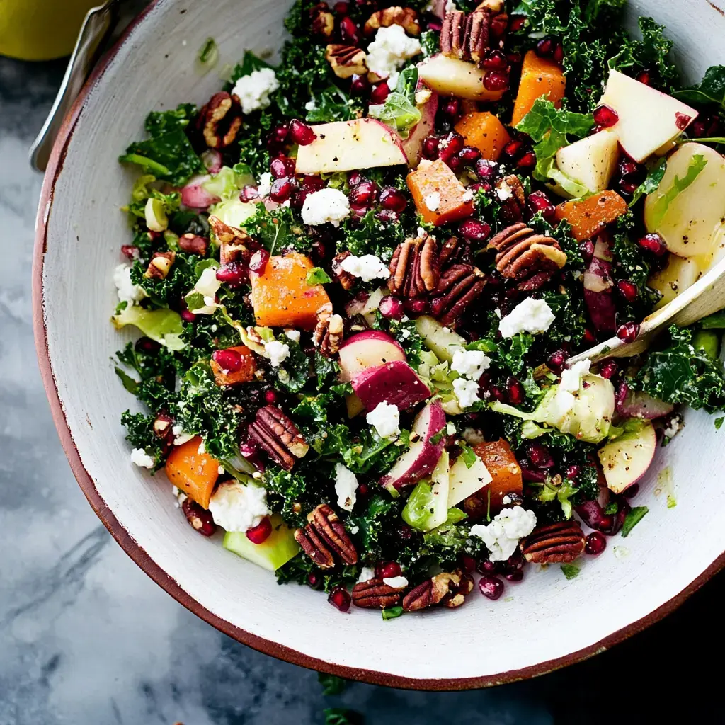 A vibrant salad filled with kale, apples, pomegranate seeds, pecans, and feta cheese, served in a wooden bowl.