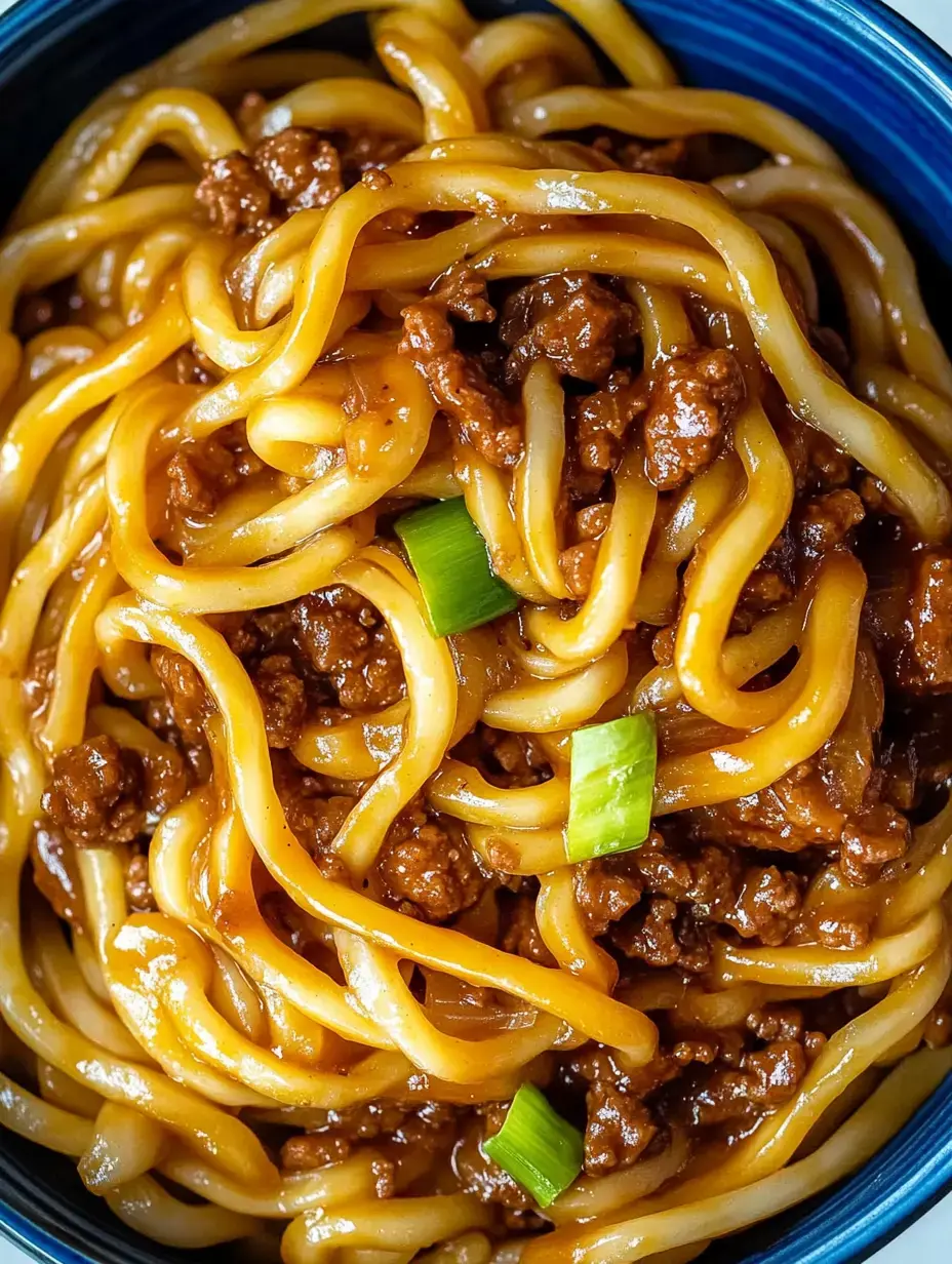 A close-up of a bowl of noodles topped with ground meat and garnished with green onions.