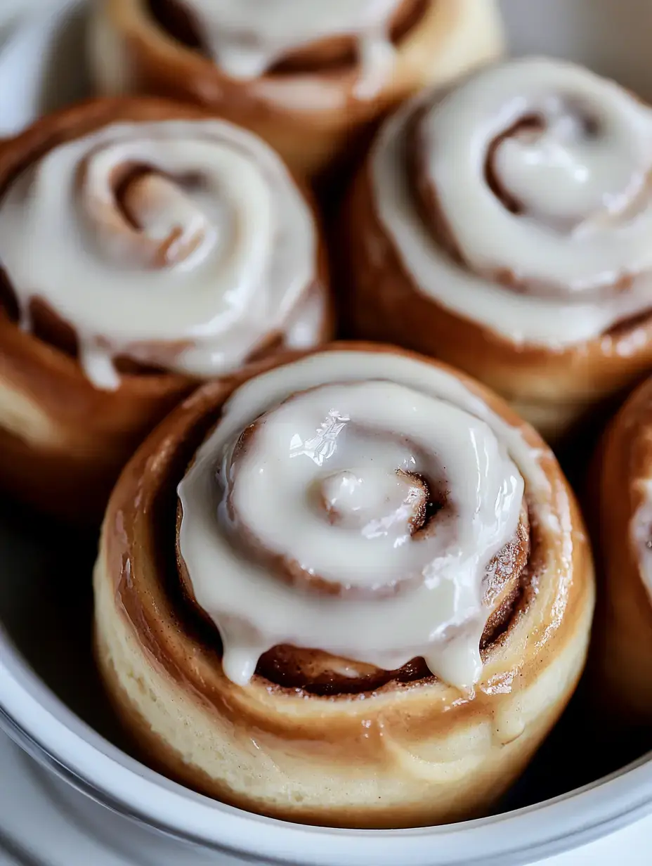 A close-up of freshly baked cinnamon rolls topped with white icing in a round dish.