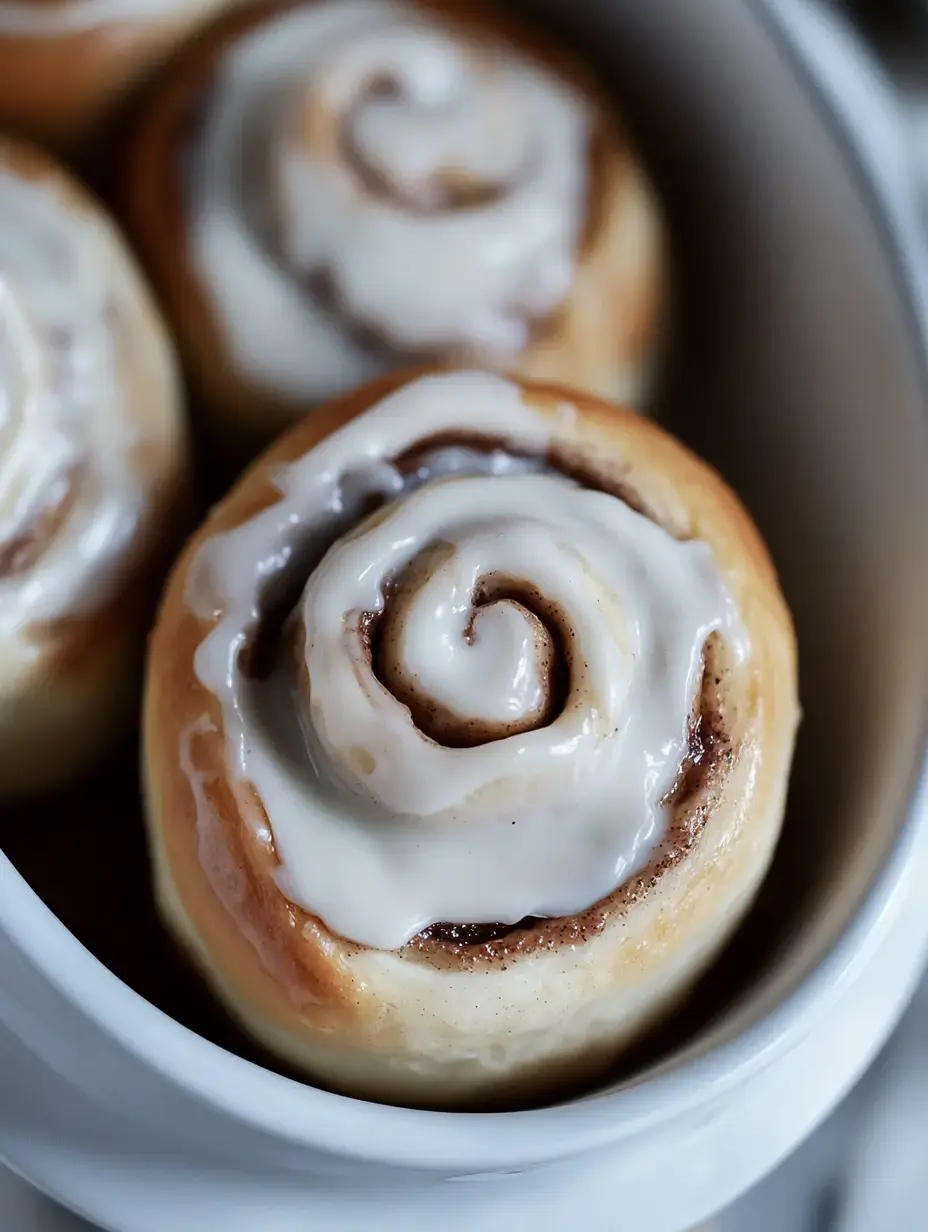 A close-up view of cinnamon rolls topped with white icing in a serving dish.