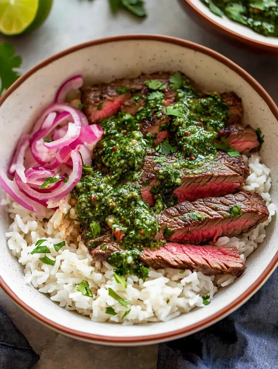 A bowl of rice topped with sliced steak, chimichurri sauce, garnished with cilantro and red onions.