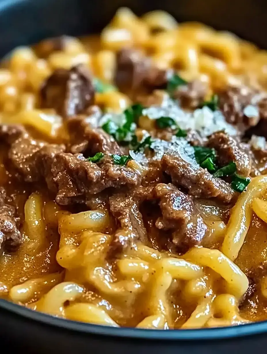 A close-up of a bowl of creamy pasta topped with tender beef and sprinkled with green herbs.