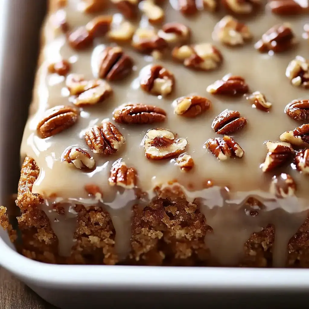 A moist cake topped with a creamy glaze and garnished with toasted pecans.