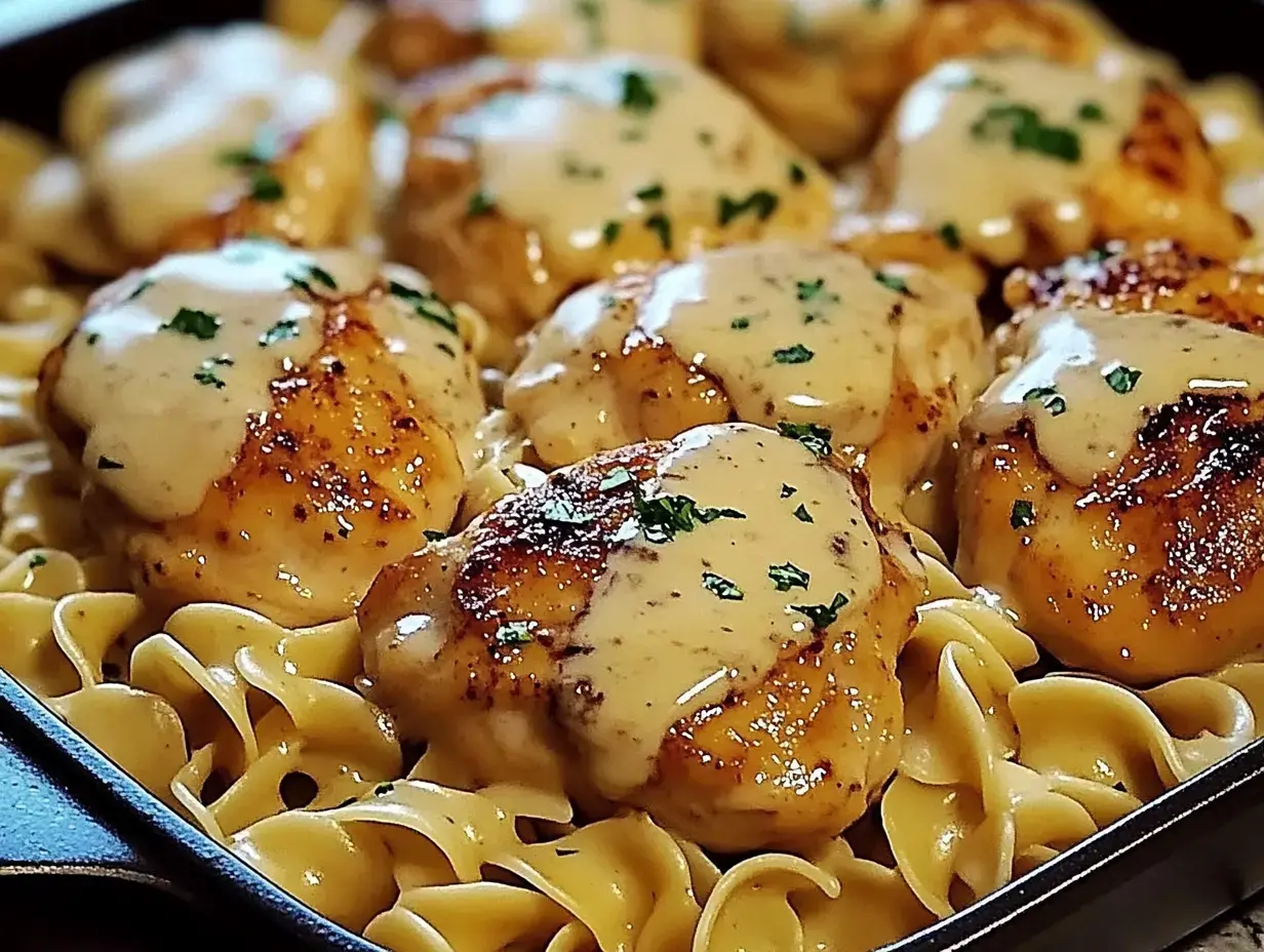 A skillet filled with egg noodles topped with sautéed chicken thighs covered in a creamy sauce and garnished with parsley.