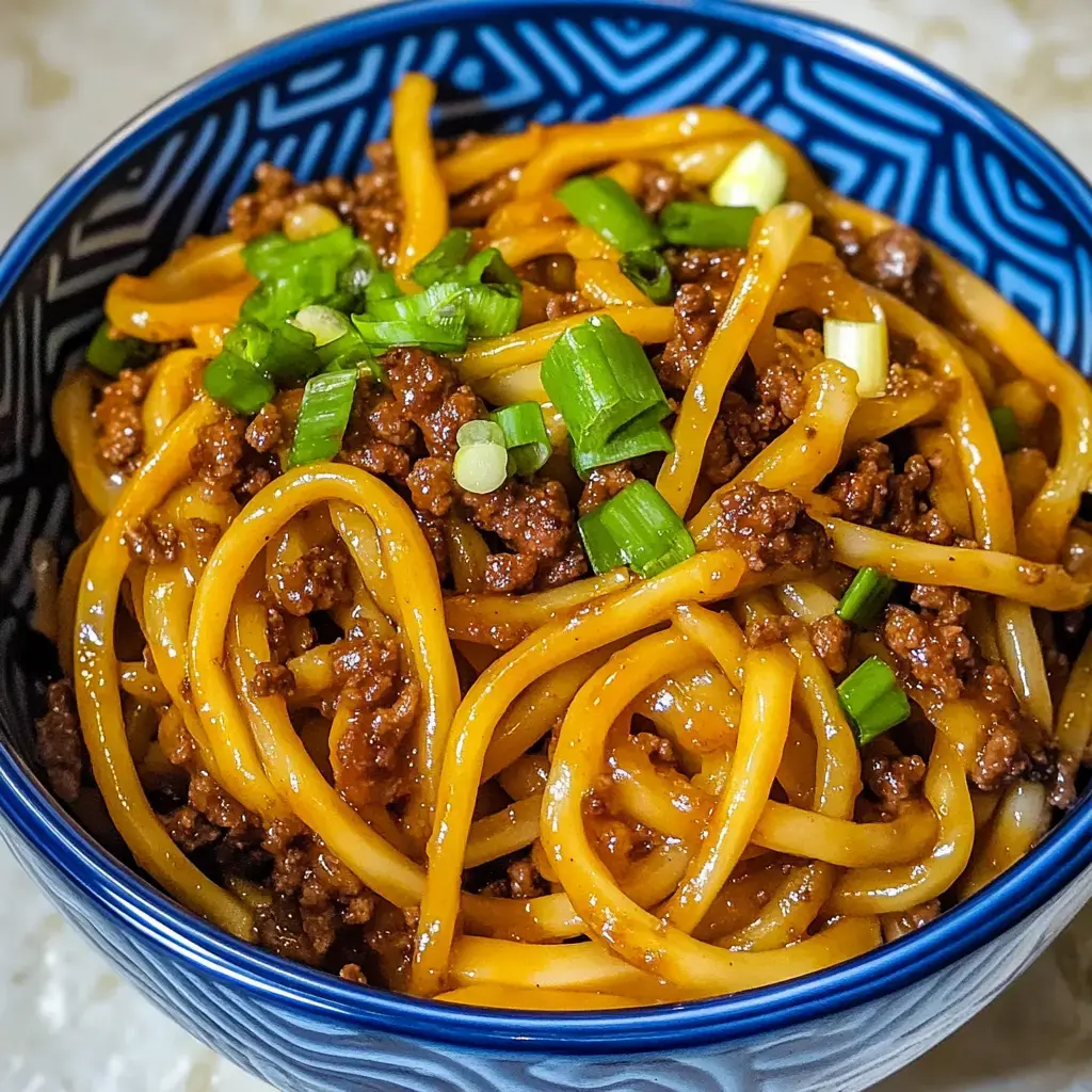 A bowl of noodles topped with minced meat and chopped green onions.