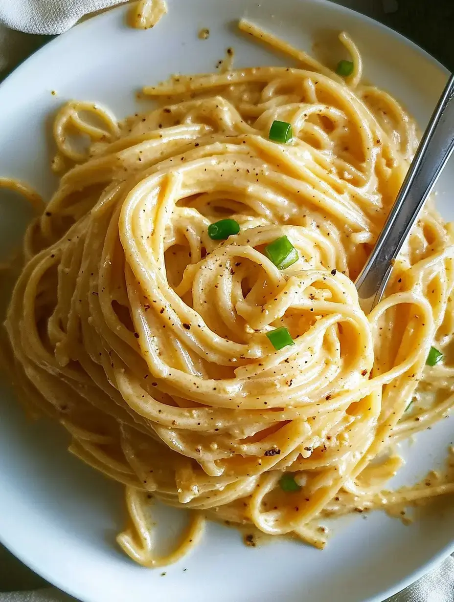 A plate of creamy pasta with green onions sprinkled on top is shown, accompanied by a fork.