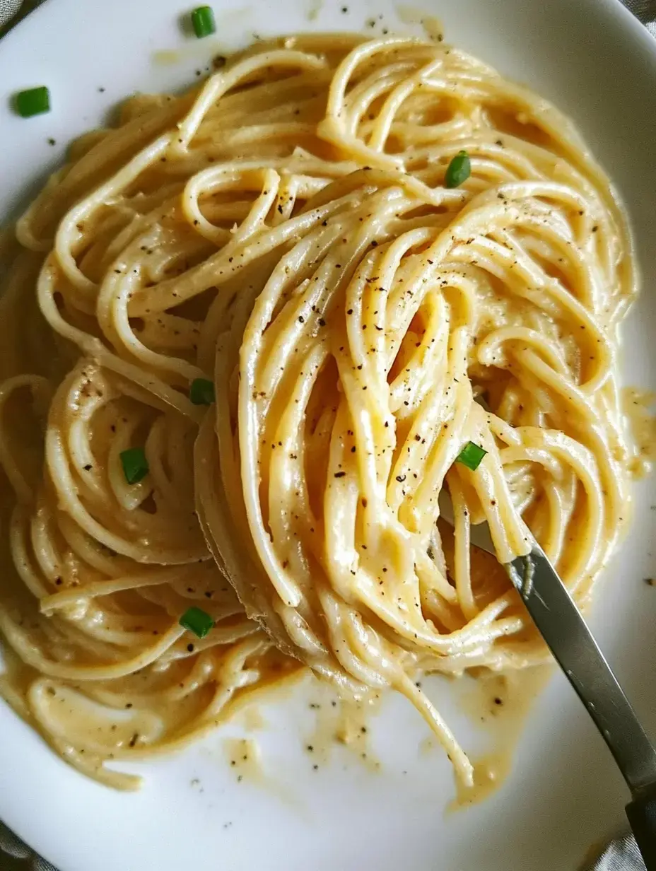 A plate of creamy spaghetti pasta garnished with black pepper and chopped green onions.