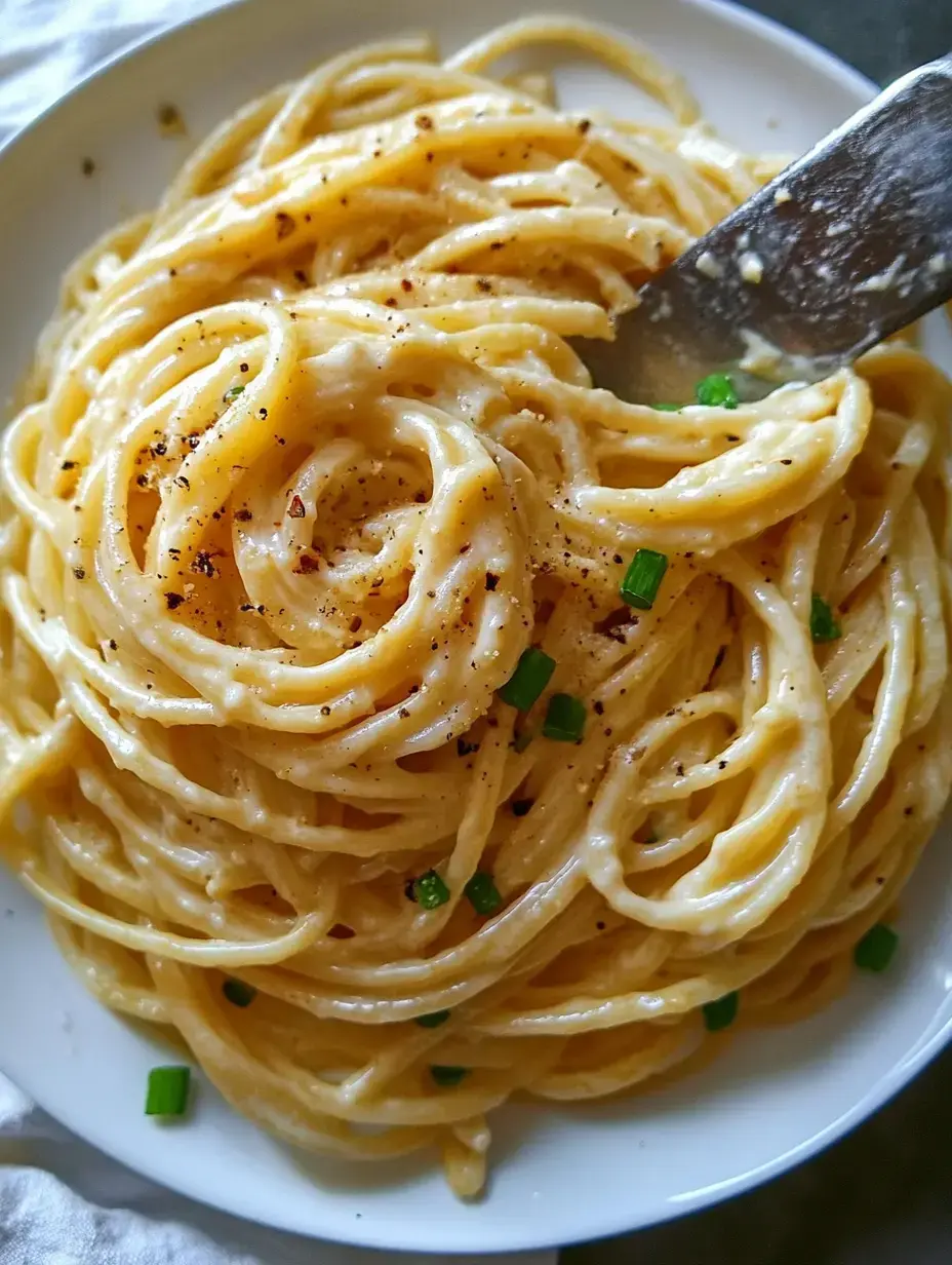 A close-up view of a plate of creamy spaghetti topped with black pepper and green onions.