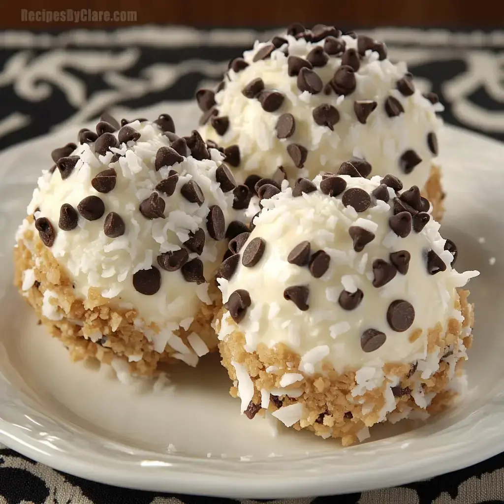 Three dessert balls coated in white frosting, sprinkled with shredded coconut and mini chocolate chips, are arranged on a decorative plate.