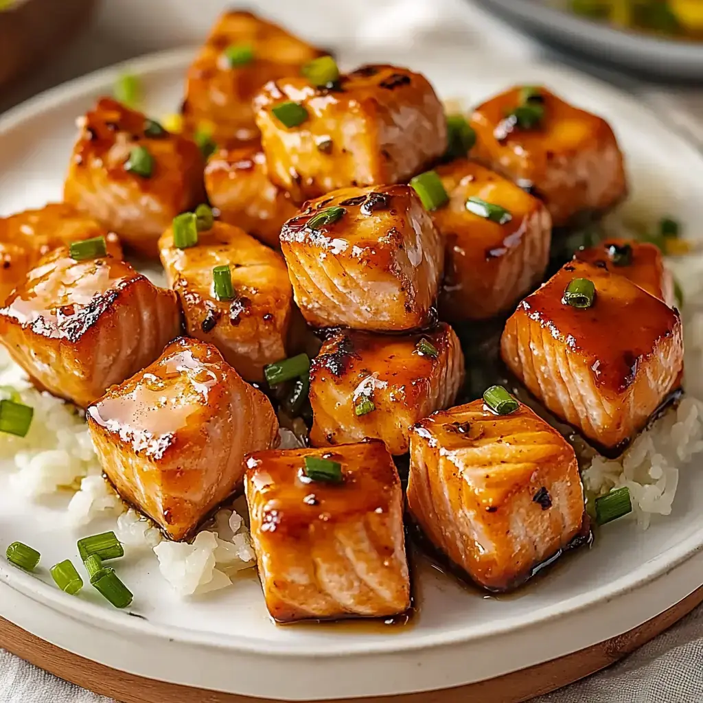 A plate of glazed salmon cubes garnished with green onions, served over a bed of rice.