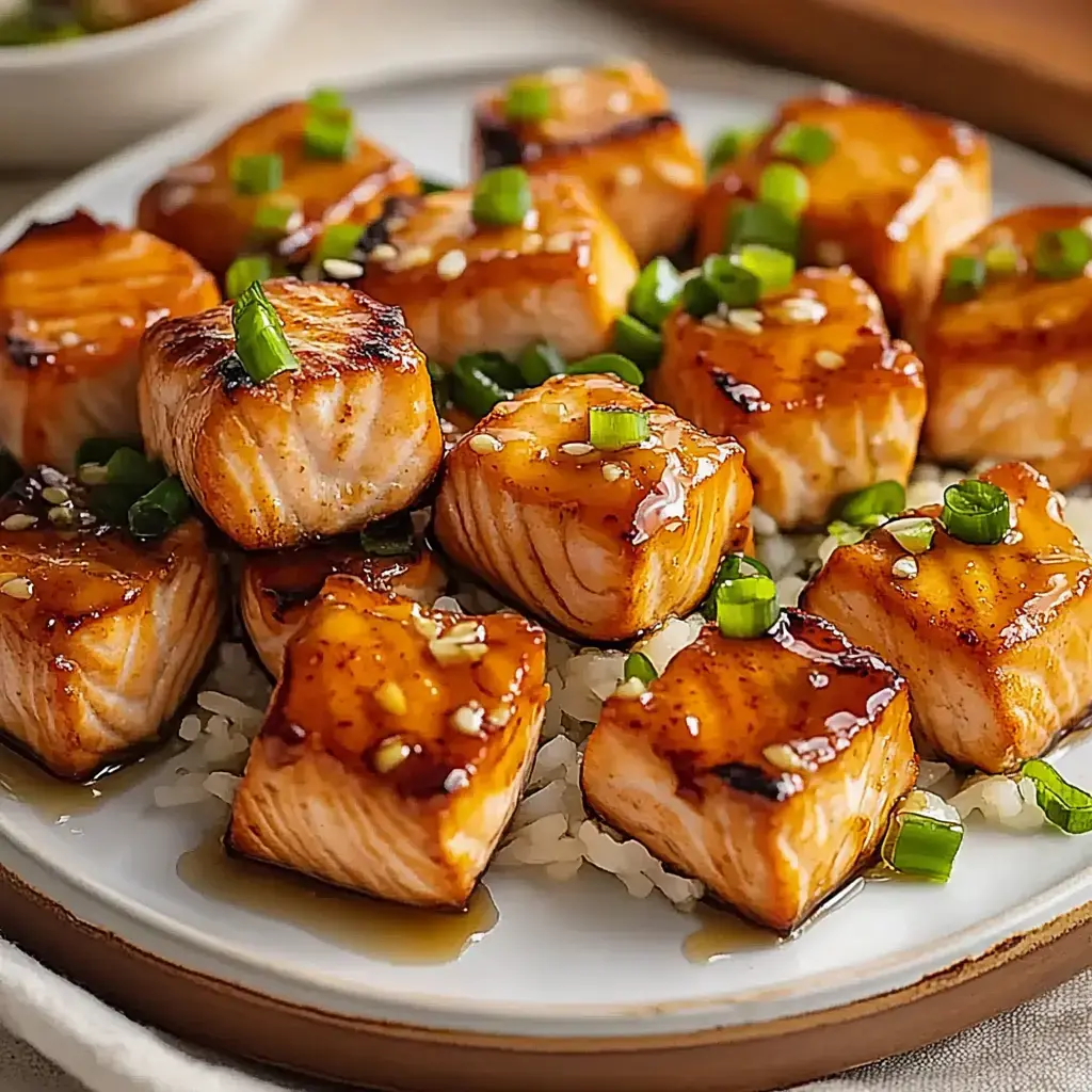 A plate of glazed, cubed salmon pieces garnished with chopped green onions, served over rice.