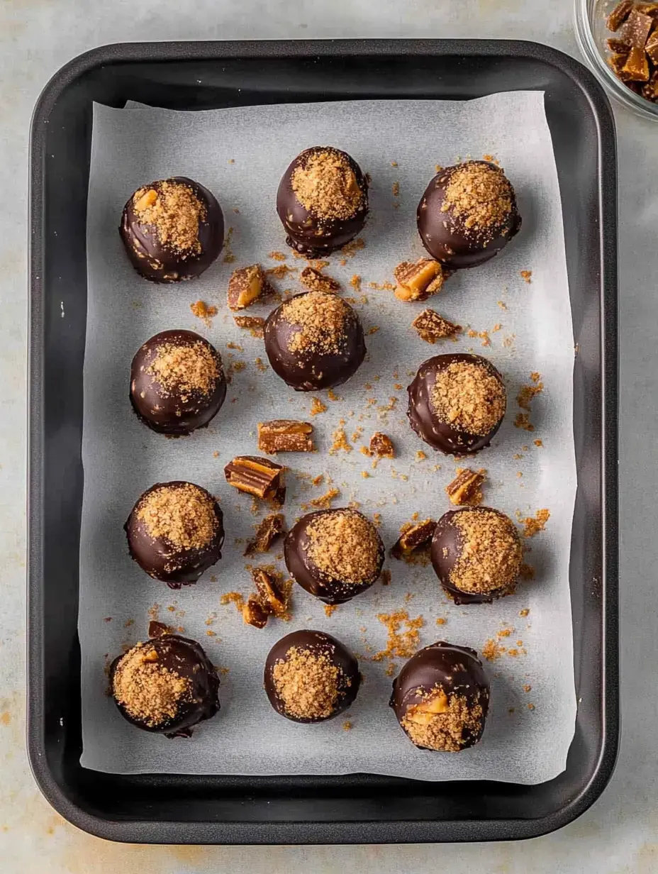 A tray of chocolate truffles topped with crushed cookies and scattered pieces of toffee.