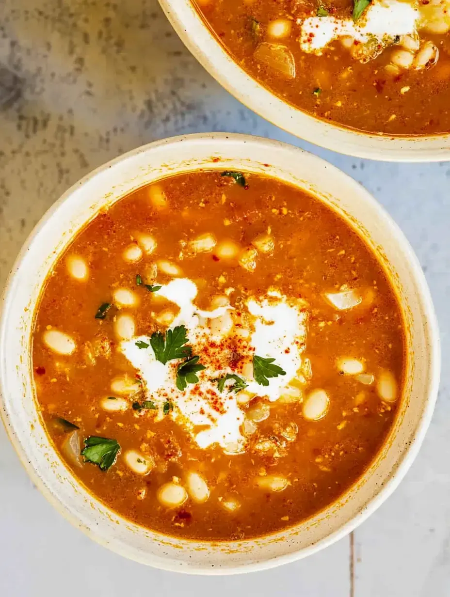 A close-up view of two bowls of soup topped with sour cream, parsley, and a sprinkle of seasoning.