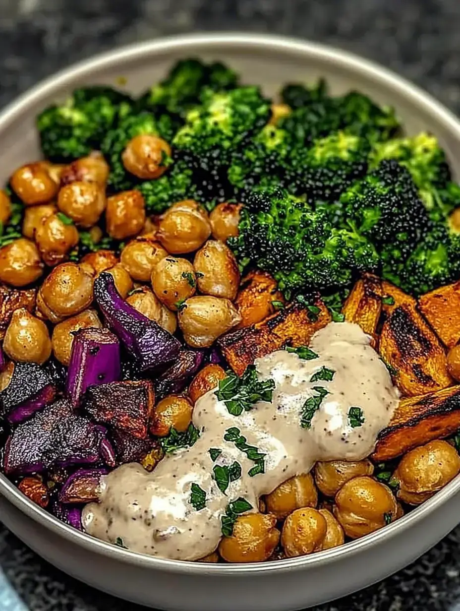 A bowl filled with roasted chickpeas, broccoli, purple sweet potatoes, and a creamy sauce, garnished with herbs.