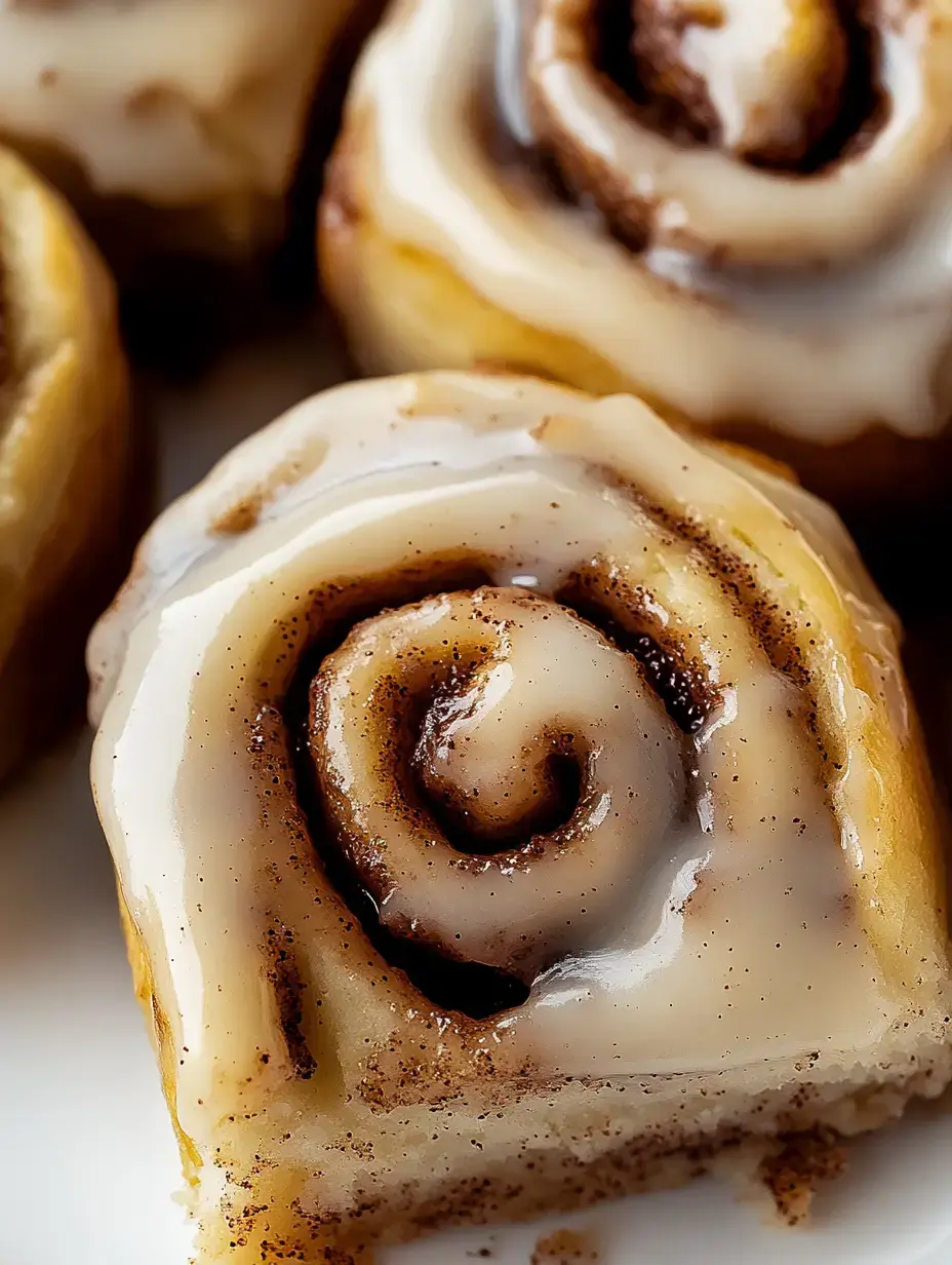 A close-up of a cinnamon roll drizzled with creamy icing, showcasing its spiral layers and a sprinkle of cinnamon.