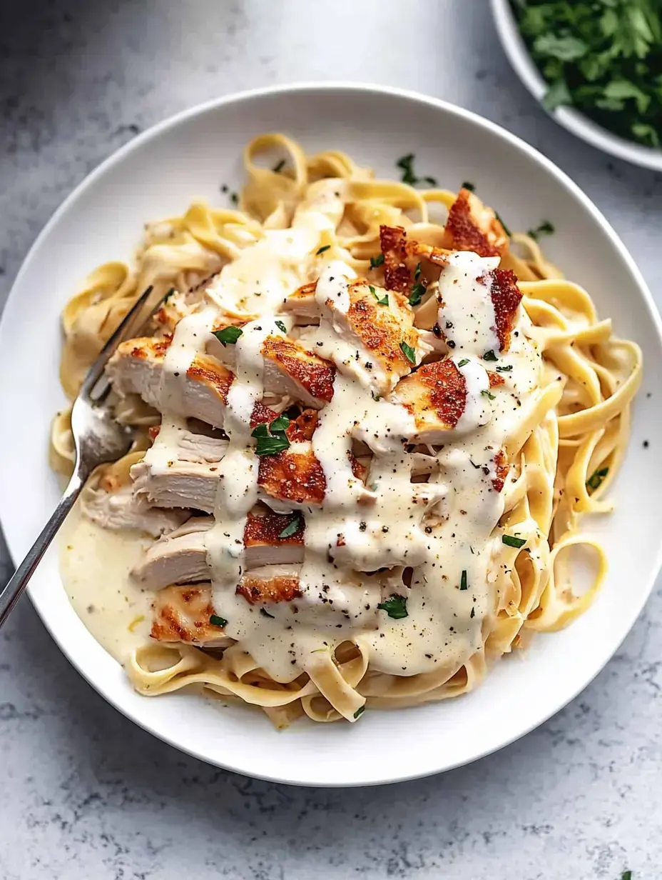 A serving of fettuccine pasta topped with sliced grilled chicken and creamy sauce, garnished with parsley.