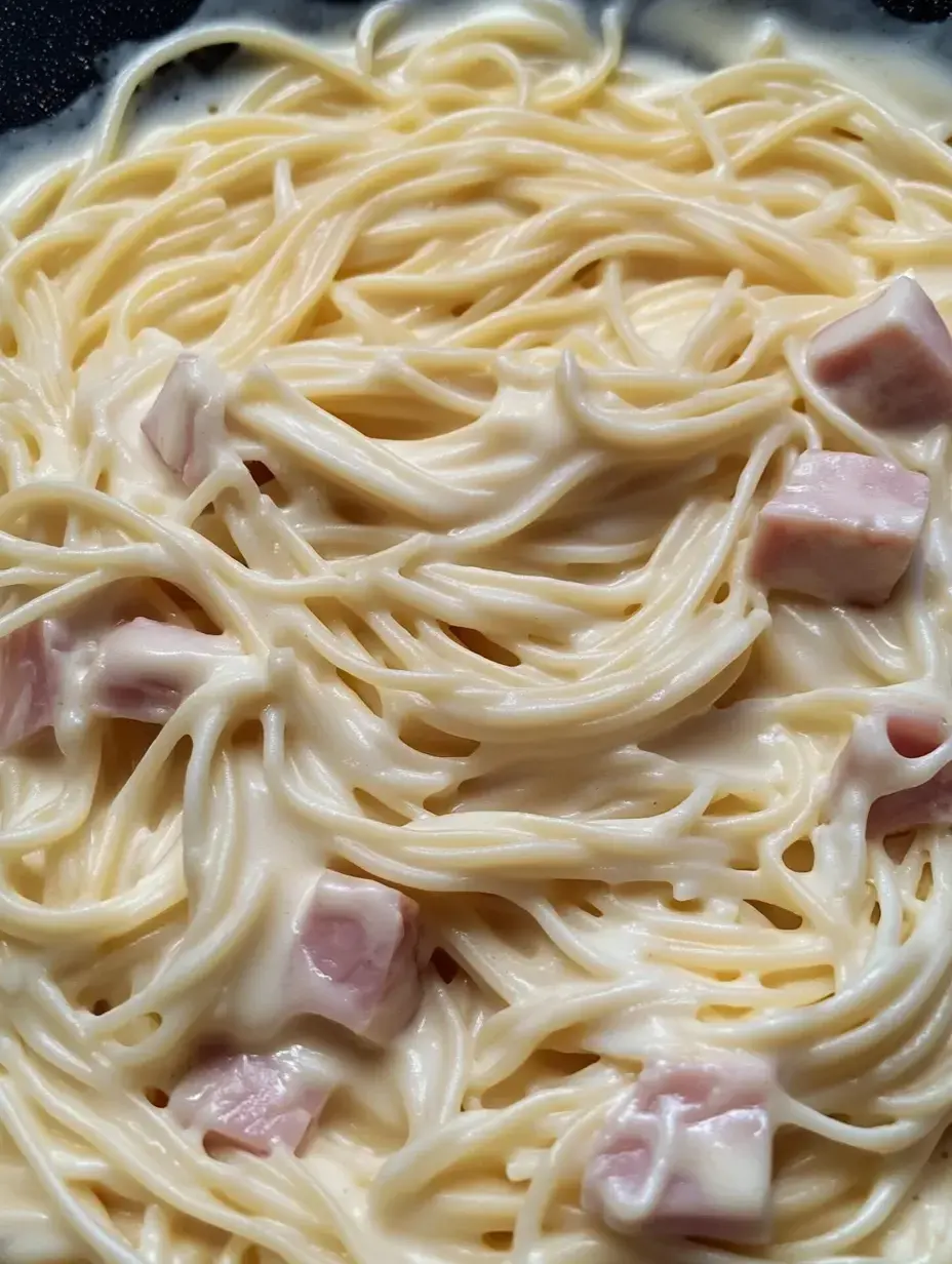 A close-up of creamy spaghetti mixed with diced ham in a light sauce.