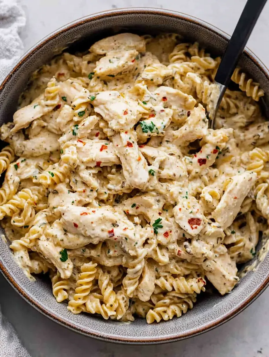 A bowl of creamy chicken pasta with rotini noodles, garnished with herbs and spices.