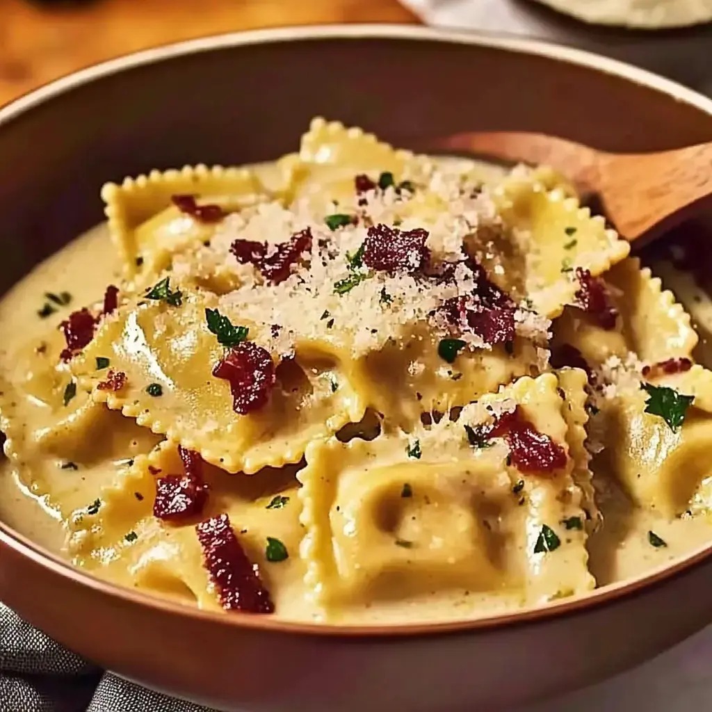 A bowl of ravioli in a creamy sauce topped with bacon bits and grated cheese.