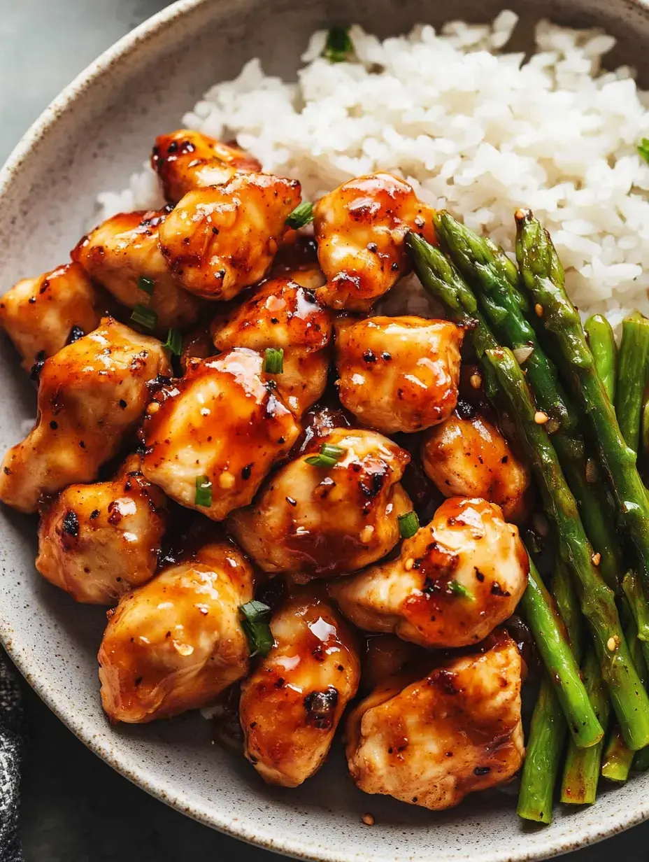 A bowl of glazed chicken pieces served with white rice and asparagus.