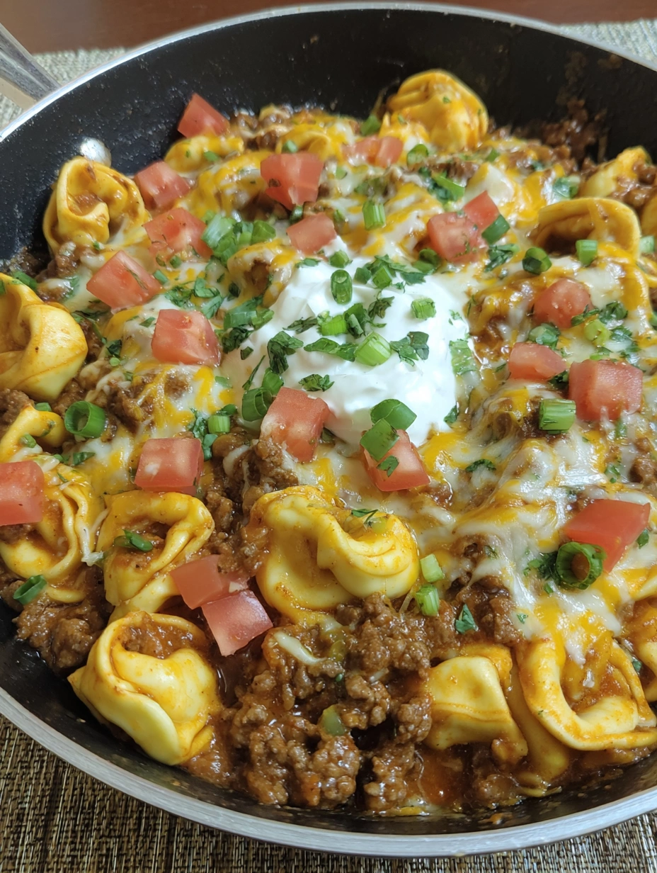 Cheesy taco tortellini skillet with seasoned ground beef, red enchilada sauce, melted Colby Jack, and green onions