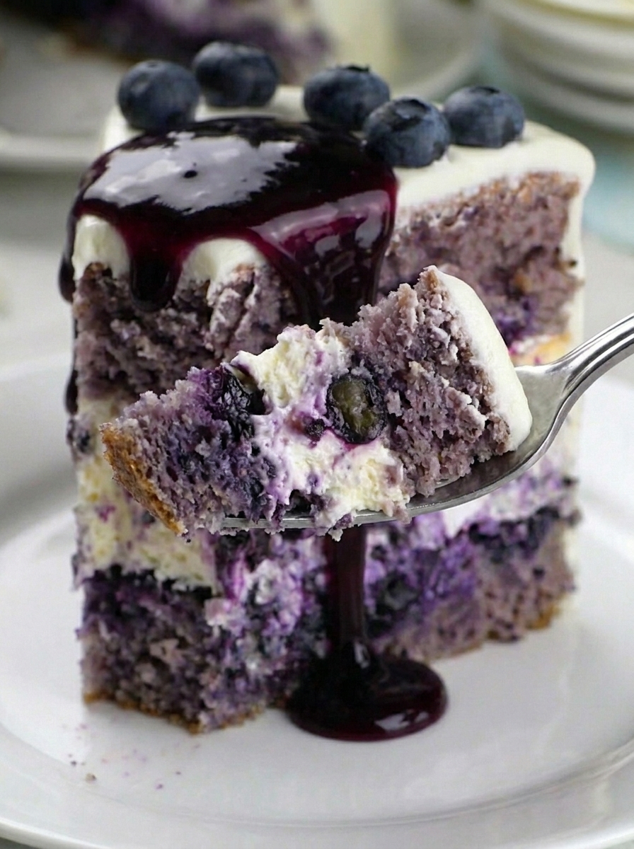 A slice of blueberry cheesecake cake with two cake layers, cheesecake center, and cream cheese frosting