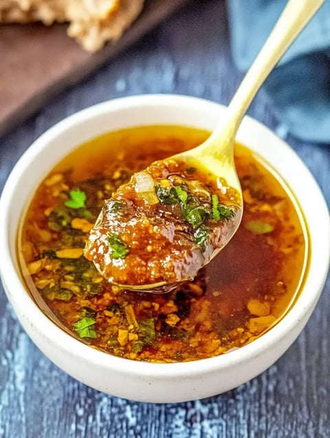 A spoonful of a flavorful green sauce with herbs and spices is lifted from a small white bowl.