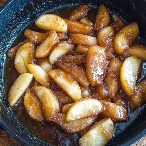 A close-up of caramelized apple slices coated in a glossy sauce, served in a dark pan.