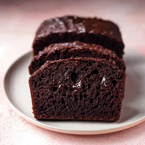 A close-up view of three slices of rich, chocolate cake on a round plate, showcasing a moist and glossy texture.